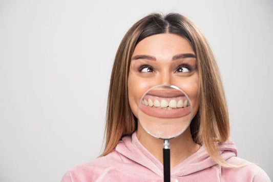 A girl holding a magnifying glass, showing a close-up of her front teeth