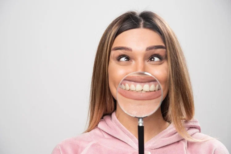 A girl holding a magnifying glass, showing a close-up of her front teeth