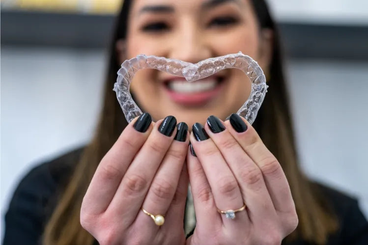 A girl making a heart with two clear aligners