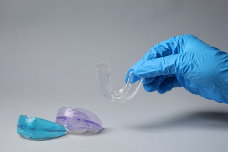 A dentist holding a mouth guard, with 2 mouth guards on the side. 