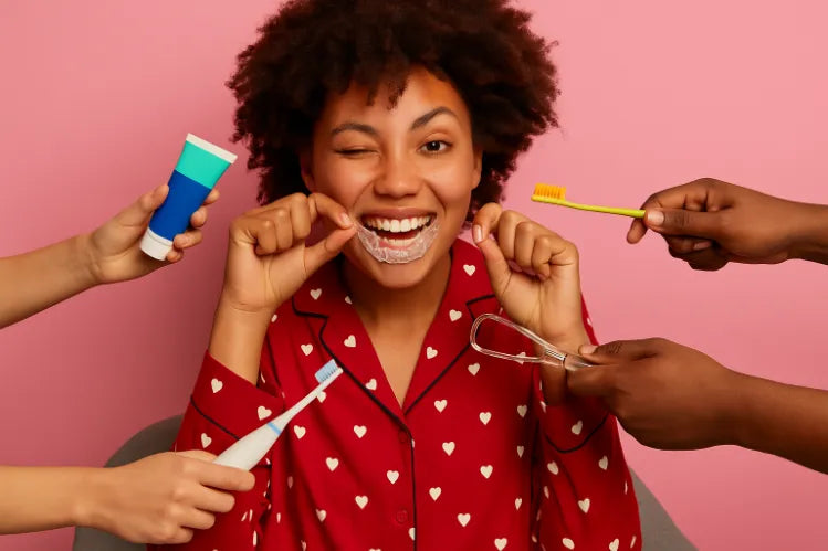A girl smiling and holding a clear aligner near her mouth, surrounded by multiple hands offering dental tools and toothpaste