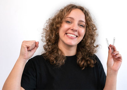A girl smiling while holding an aligner in her hand