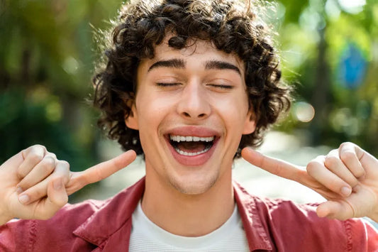 Curly-haired young man smiling while playfully pointing towards his smile with index fingres