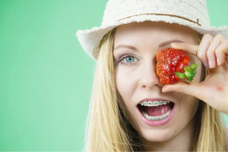 A girl wearing braces and holding up a strawberry