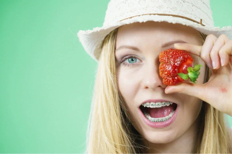 A girl wearing braces and holding up a strawberry
