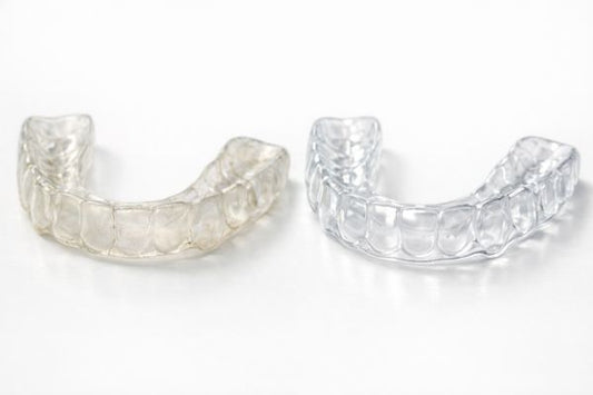 A yellowed dental night guard and a brand-new, clear replacement night guard.