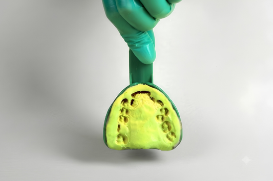 A hand in green gloves holding a dental impression tray filled with yellow impression material.
