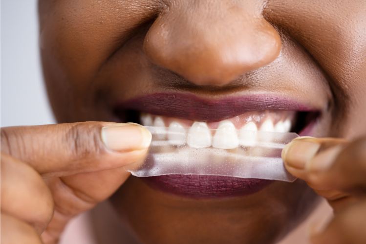 A person putting on a teeth whitening strip on their teeth. 