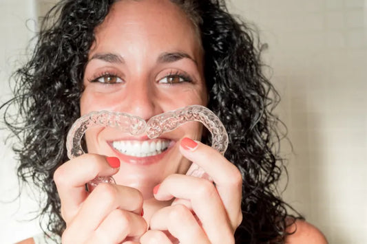  A girl smiling with aligned teeth while making a heart out of aligners