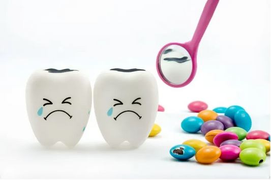 Two cartoon teeth with sad faces and cavities, surrounded by colorful candies and a pink dental mirror showing decay